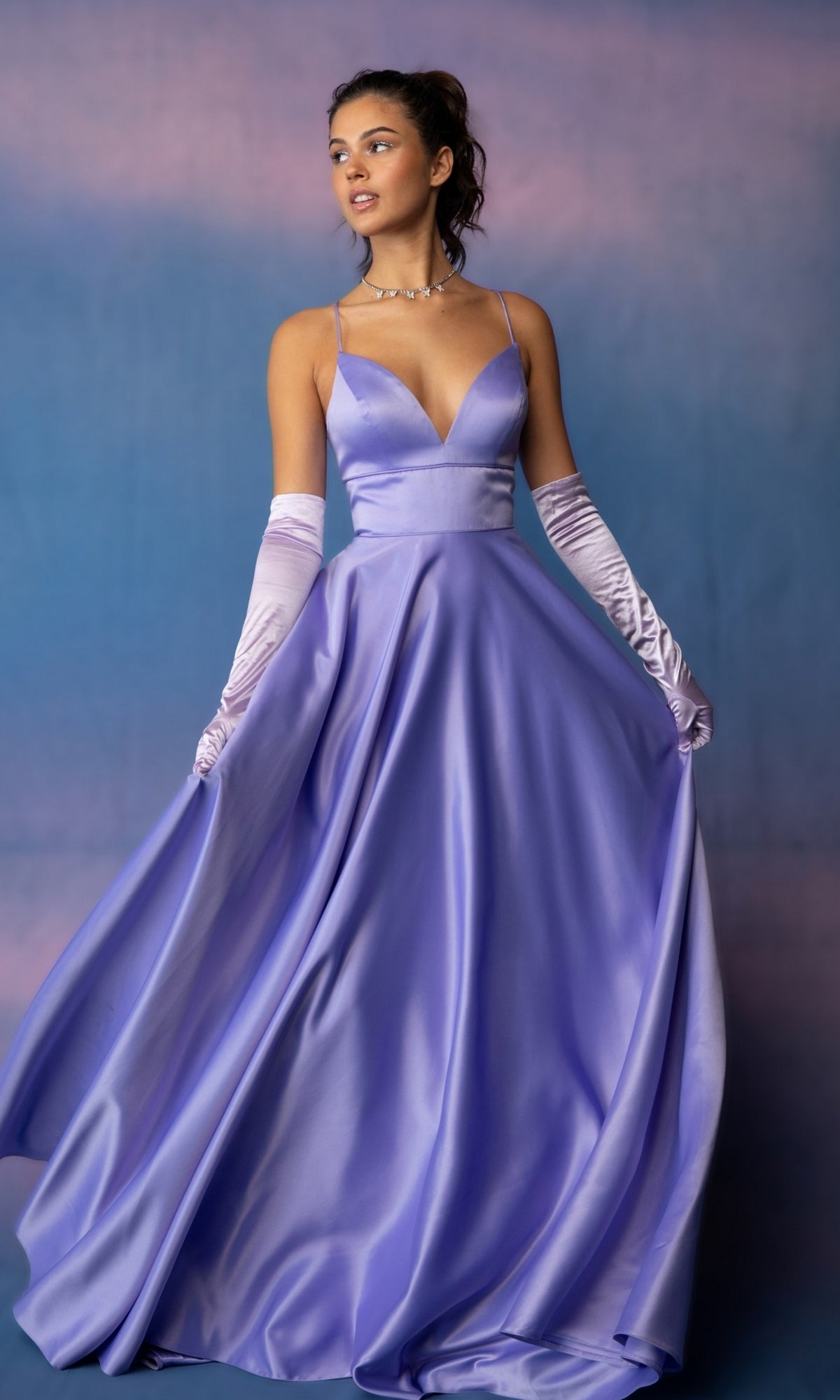 A person wearing a lavender Strappy-Back Long Satin Prom Dress: Eureka 9008 with a plunging neckline and matching opera-length gloves, holding the skirt of the long satin dress out to the sides.